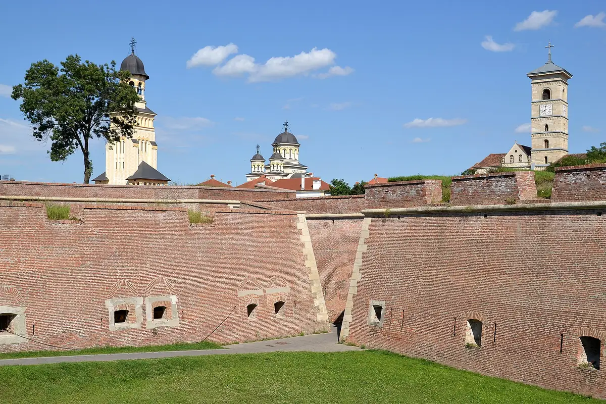 The angled brick walls and gun loopholes of the Alba Carolina ditch, with the bell tower of the Coronation Cathedral and the clock tower of St Michael cathedral rising behind them