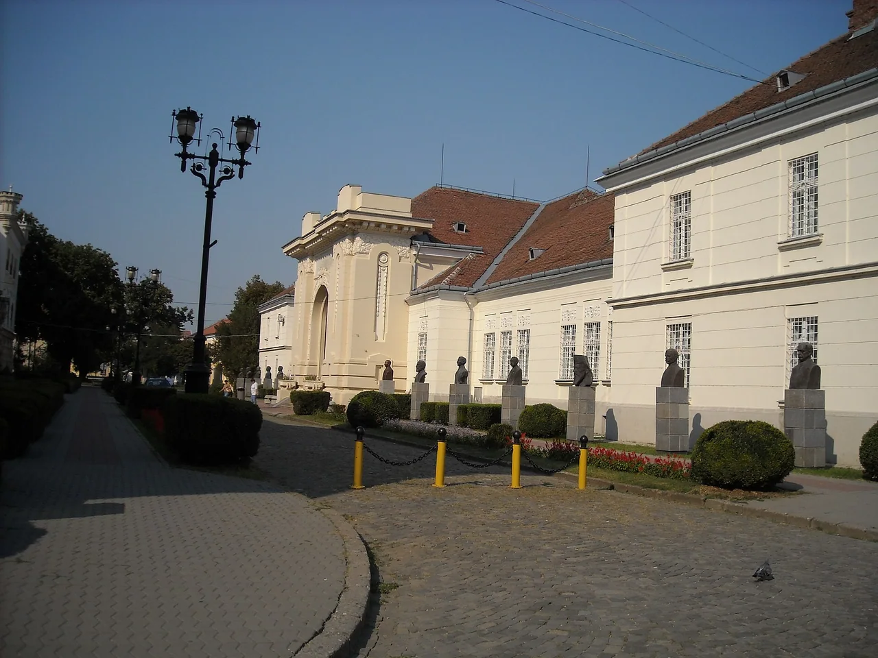 The Union Hall in Alba Iulia, a long cream-coloured building with a tall arched portico, fronted by an alley of bronze busts on stone plinths