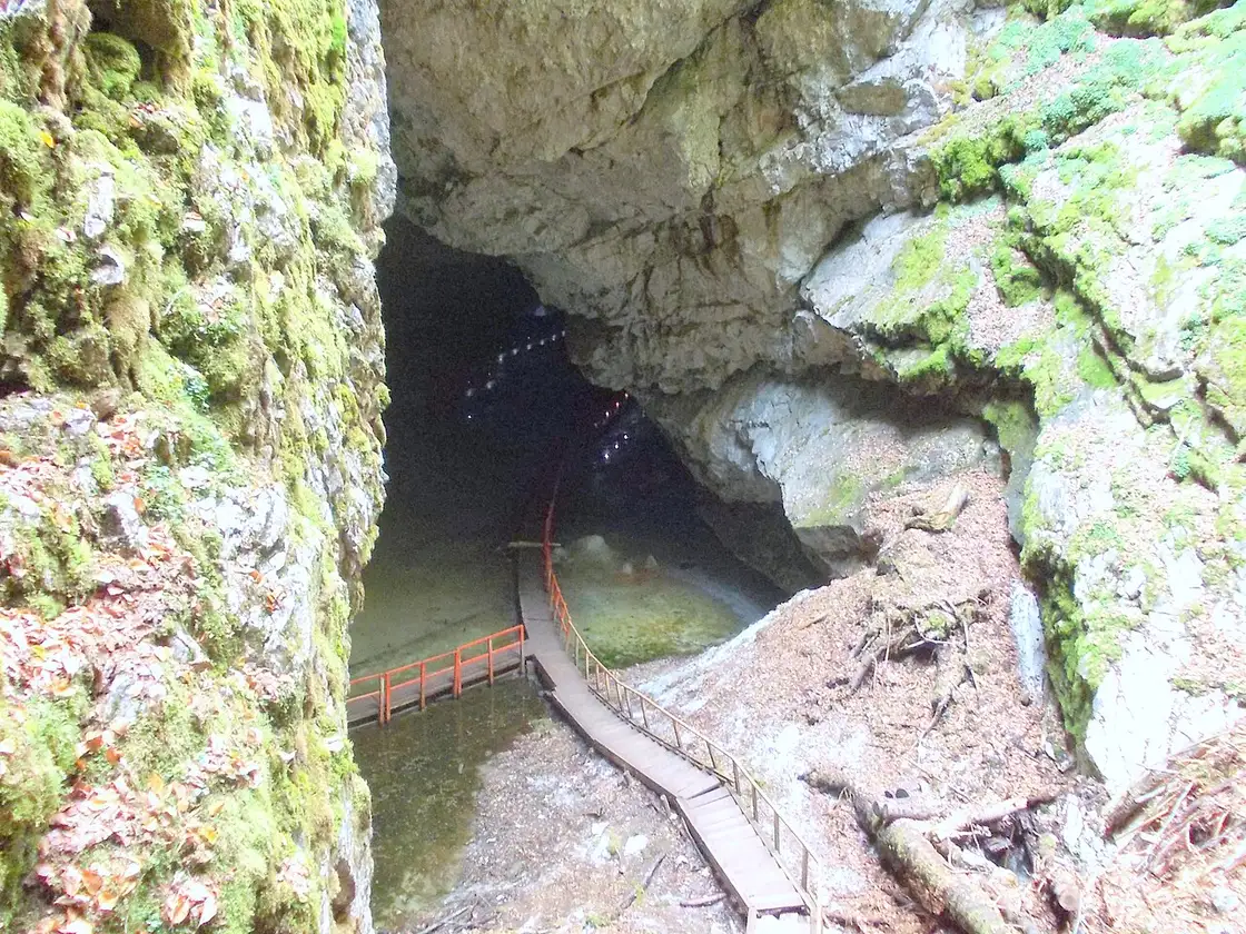 The daylight cave mouth on the Scarisoara approach in the Apuseni - a wooden boardwalk and orange railing between mossy limestone walls