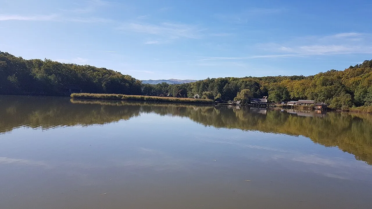 The lake at ASTRA Museum in Sibiu with wooden windmills reflected in still water and forested hills behind
