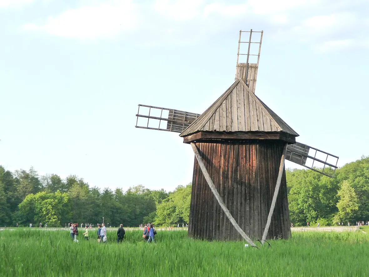 Visitors walking past a large wooden windmill in an open meadow at ASTRA Museum