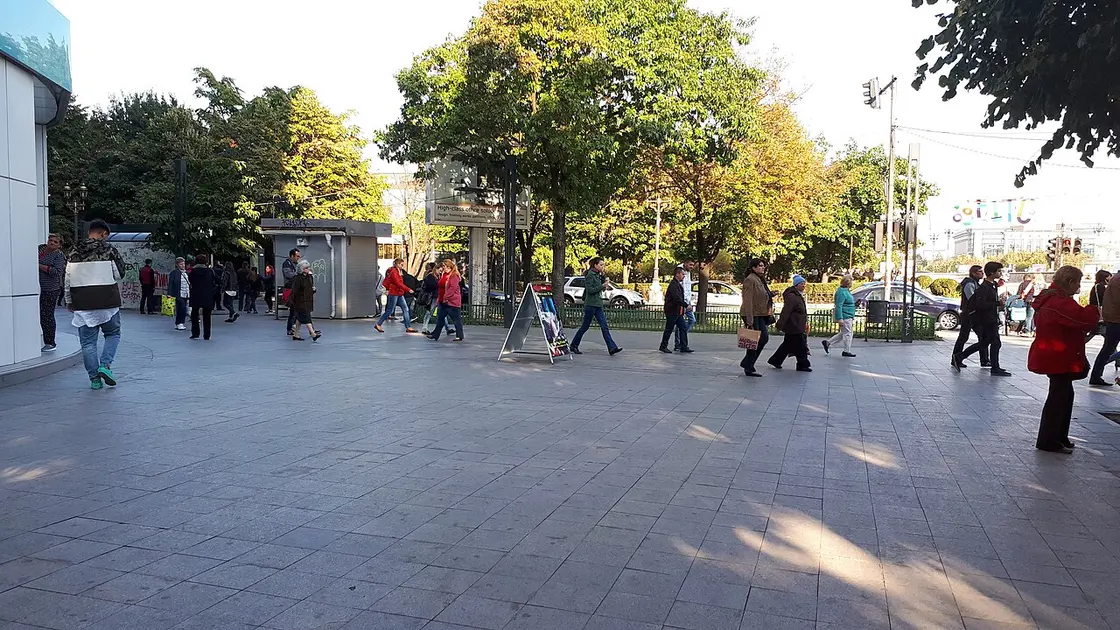 A busy pedestrian street in central Bucharest on a sunny day, crowds walking under trees, the kind of city where all three Romanian networks run fast