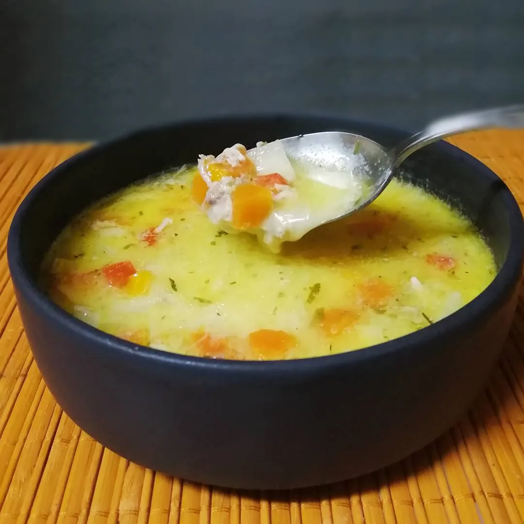 A bowl of creamy chicken ciorba radauteana topped with sour cream and herbs