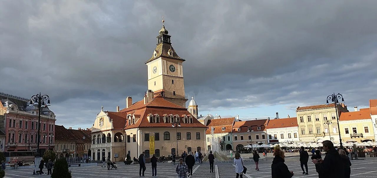 The cafe terraces of Piata Sfatului in Brasov, the baroque Council House tower rising behind the umbrellas