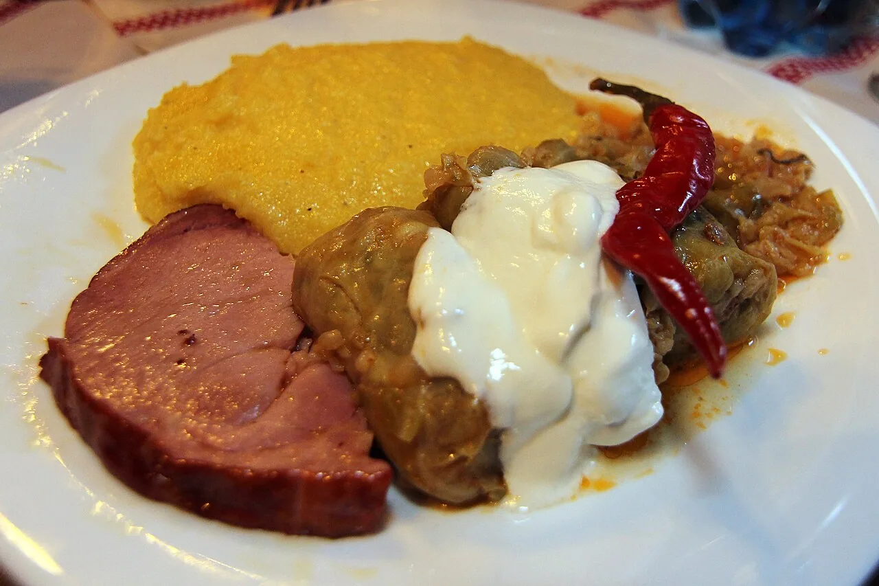 A plate of sarmale cabbage rolls with a mound of mamaliga polenta and a spoon of sour cream