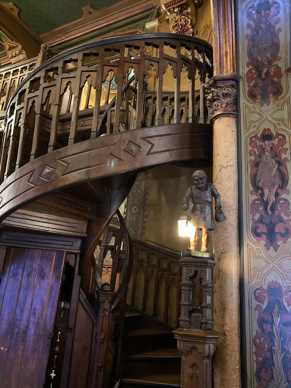 Carved wooden gallery and painted arches inside Caru cu Bere, tables set beneath ornate columns