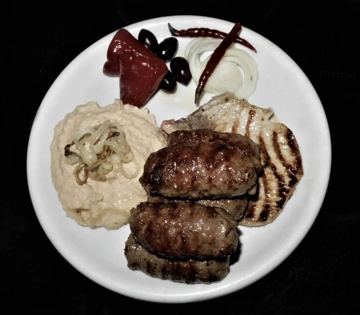 A mixed grill plate of Romanian mici and grilled meats with a scoop of bean pate
