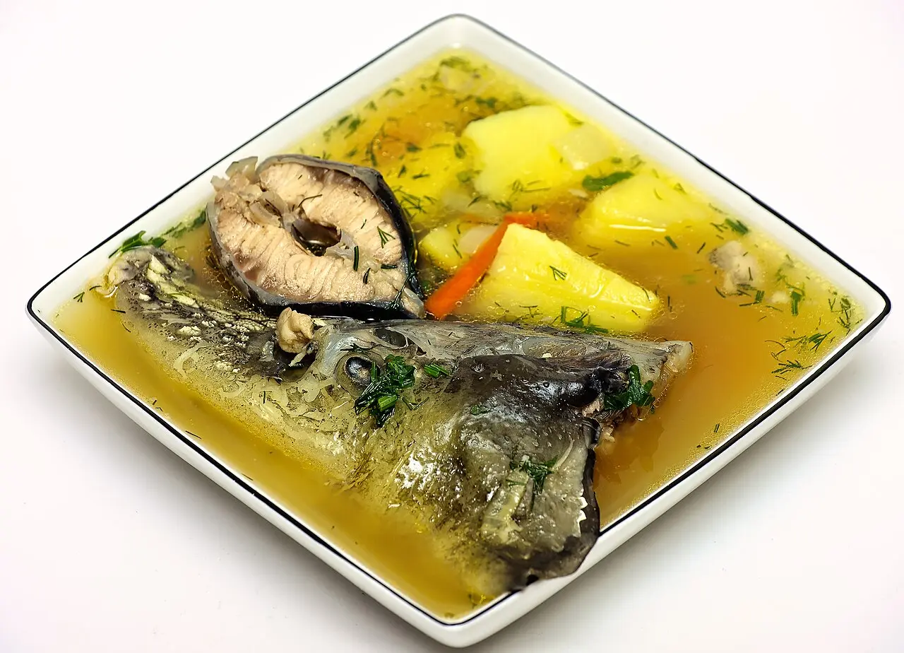 A clear bowl of fish soup with visible fish pieces, herbs and a red broth, the same style as a Lipovan-style fish soup