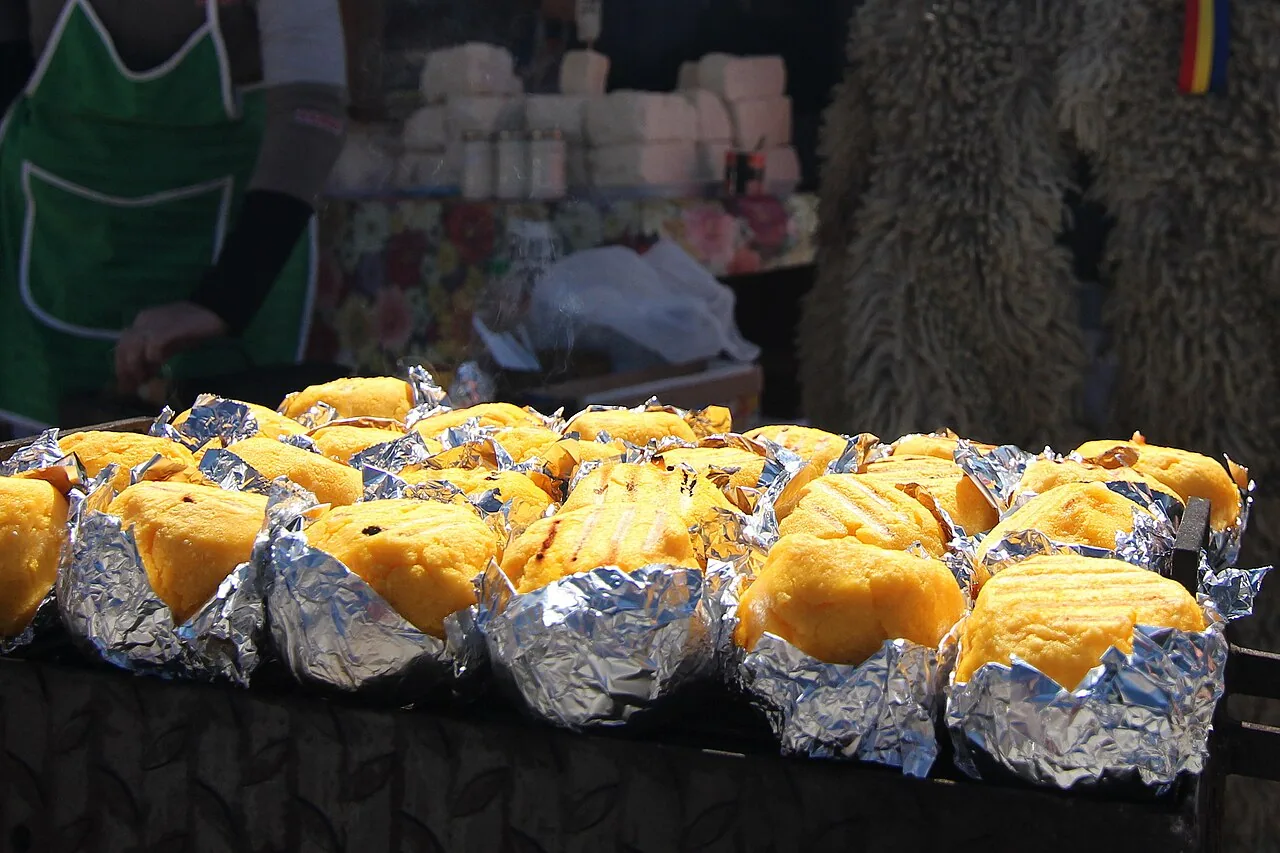 Rows of bulz, balls of polenta stuffed with cheese, grilling in foil at a market stall