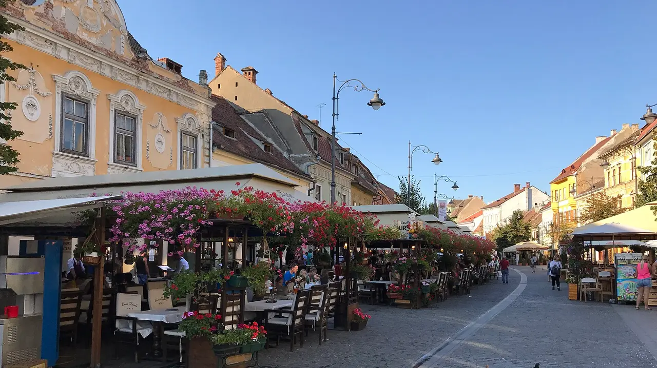 Restaurant terraces draped in geraniums along the pedestrian Strada Nicolae Balcescu in Sibiu on a summer evening