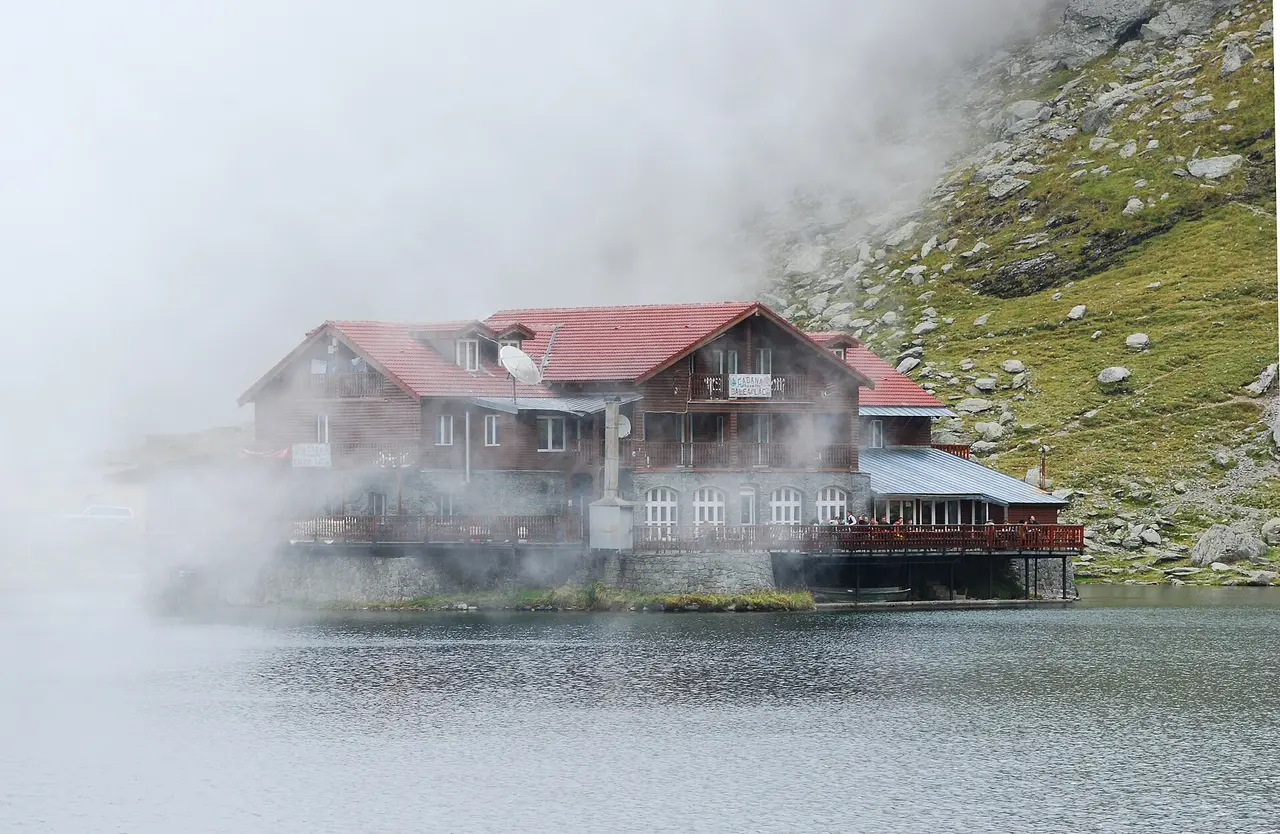 Balea Lake high on the Transfagarasan in summer, the mountain chalet reflected in the water with cloud spilling over the Fagaras ridge above