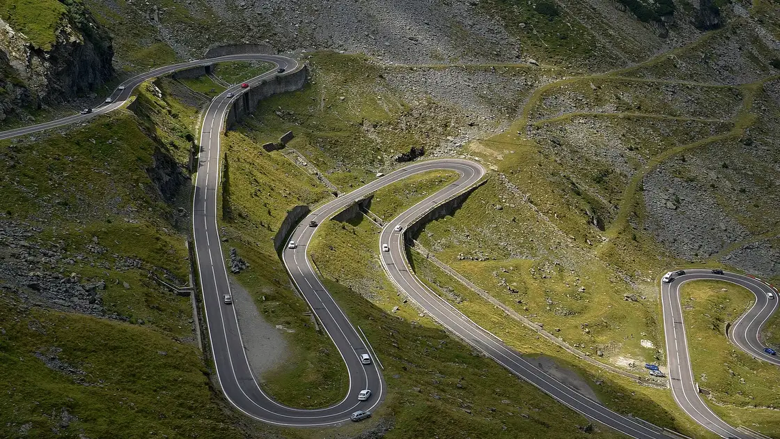 The Transfagarasan mountain road looping up the green Fagaras slopes in summer, the switchbacks that only open once the snow clears in June