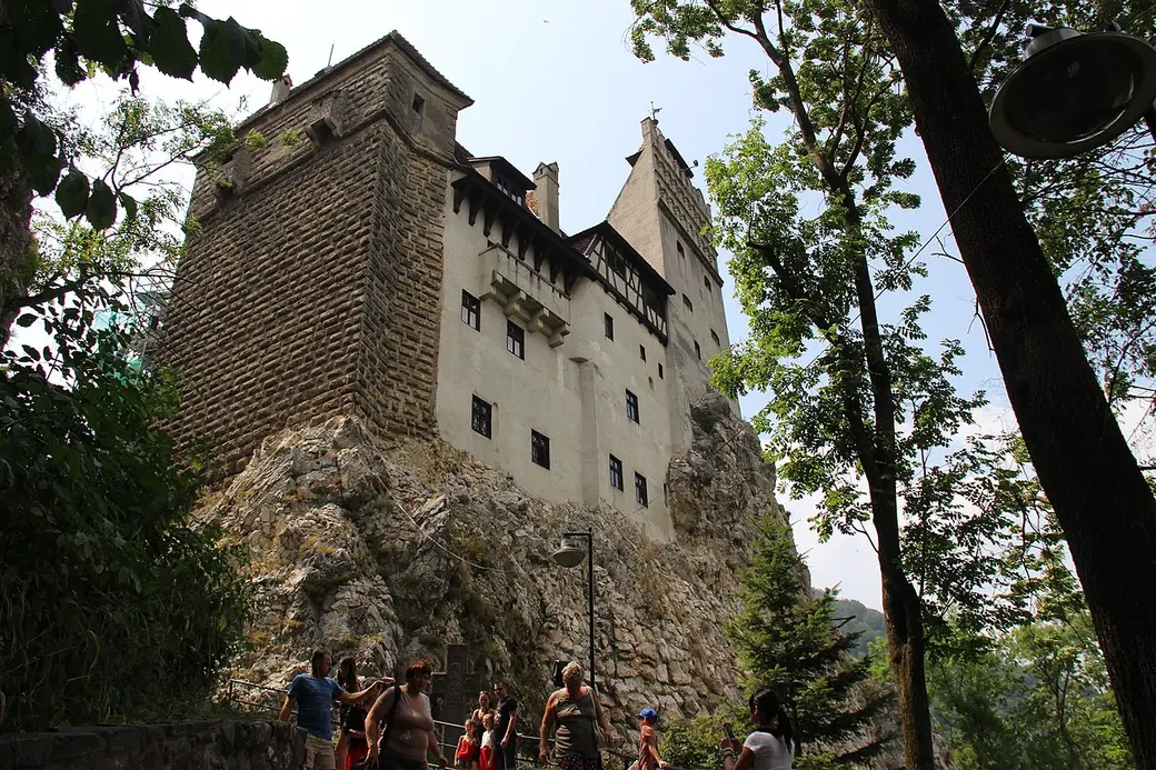 Visitors climbing the path up the rocky base of Bran Castle, the towers rising steeply above them