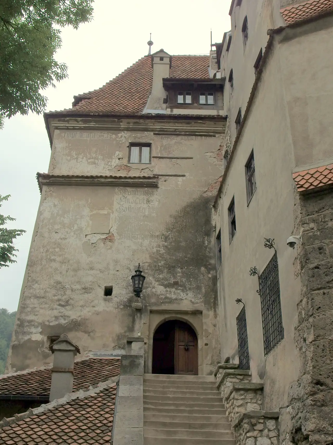 The tight inner courtyard of Bran Castle with a stone well, tiled roofs and white towers rising above