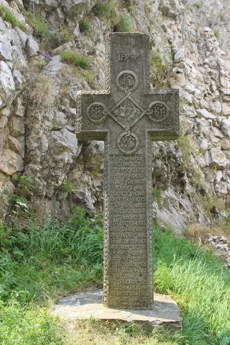 A carved stone Orthodox cross with Cyrillic inscription set against the rock at the foot of Bran Castle