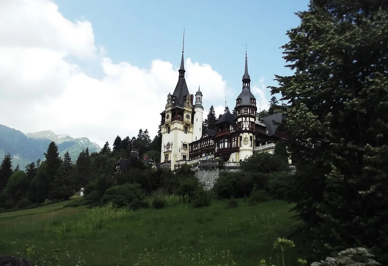 Peles Castle in Sinaia, its pale towers and grey spires rising above a green lawn with the Carpathian mountains behind