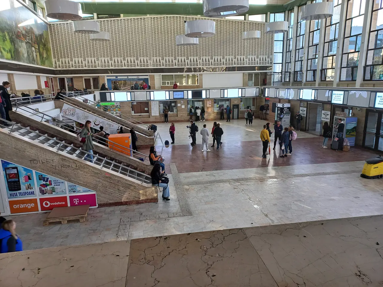 The high concourse of Brasov railway station, with ticket windows, stairs and passengers waiting under the mural