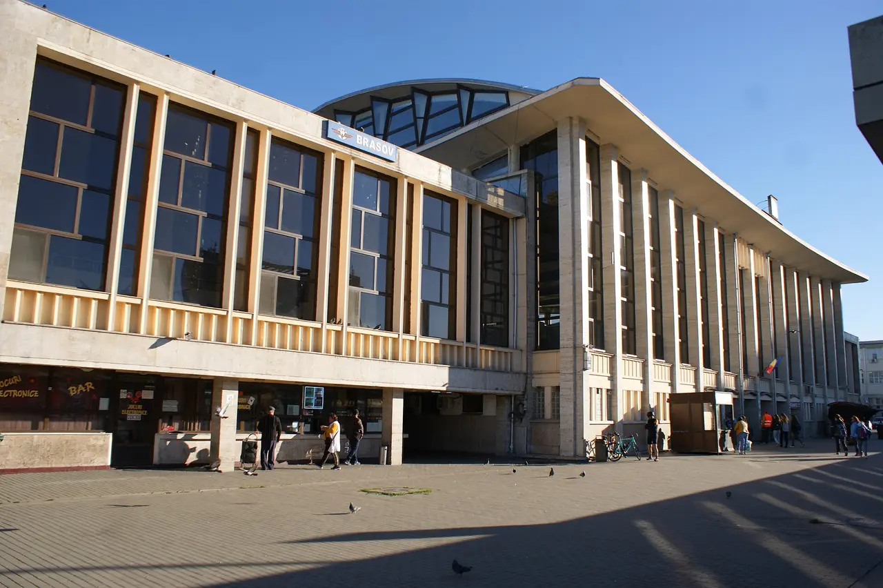 The modernist facade of Brasov railway station with the blue CFR Brasov sign above the glass front and the paved forecourt