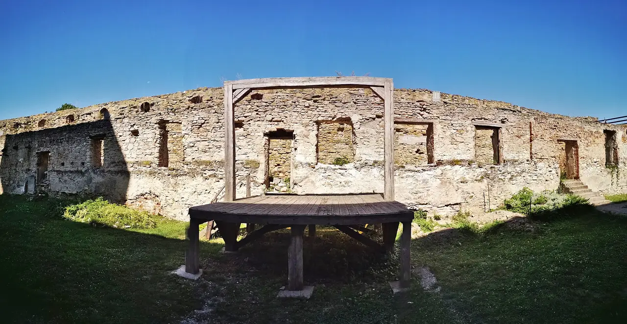 Inner courtyard of Fagaras citadel, stone walls around a grassy court with a wooden reconstruction in the foreground