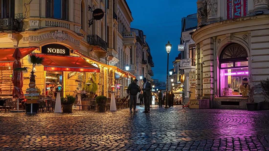 Cobbled Lipscani street in the Bucharest Old Town at blue hour, cafe terraces glowing
