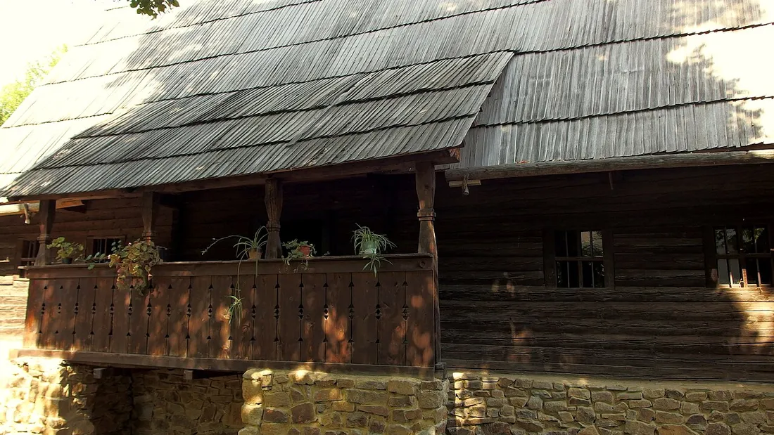 A traditional wooden peasant house with a tall shingle roof at the Village Museum in Bucharest