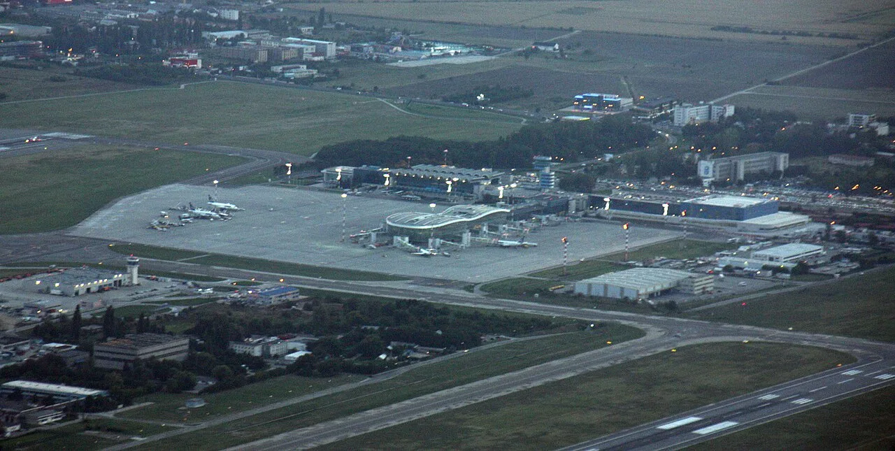 Aerial view of Bucharest Henri Coanda airport (OTP) at dusk, the terminal, aprons with parked aircraft and runways spread across the plain north of the city