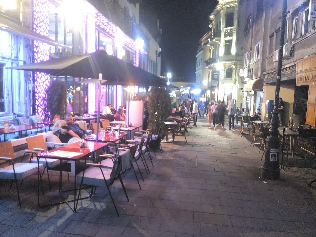 Bar terraces lit with purple and warm light along Strada Smardan in the Bucharest Old Town, people sitting out and walking the lane at night