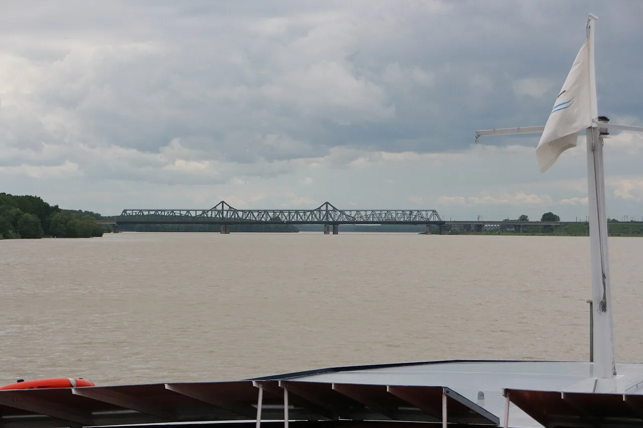 The steel truss bridge over the Danube at Cernavoda seen across the wide brown river under a cloudy sky