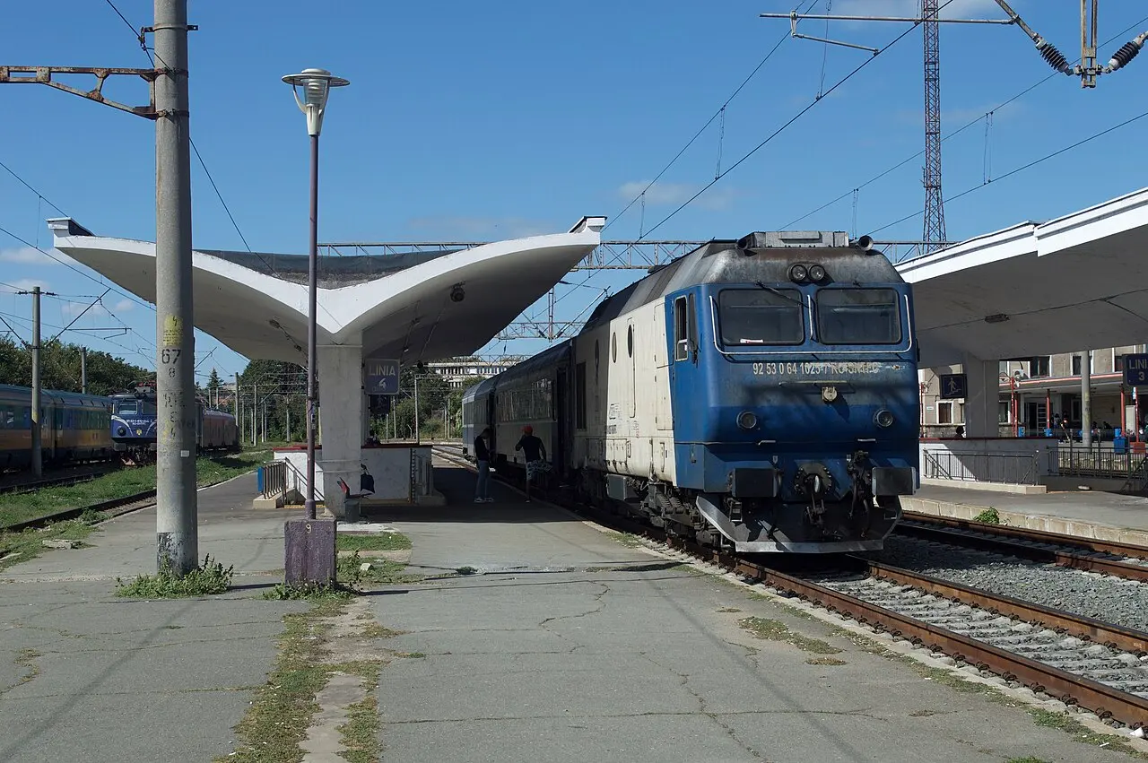 A blue and white CFR locomotive at a covered platform in Constanta, with a passenger boarding
