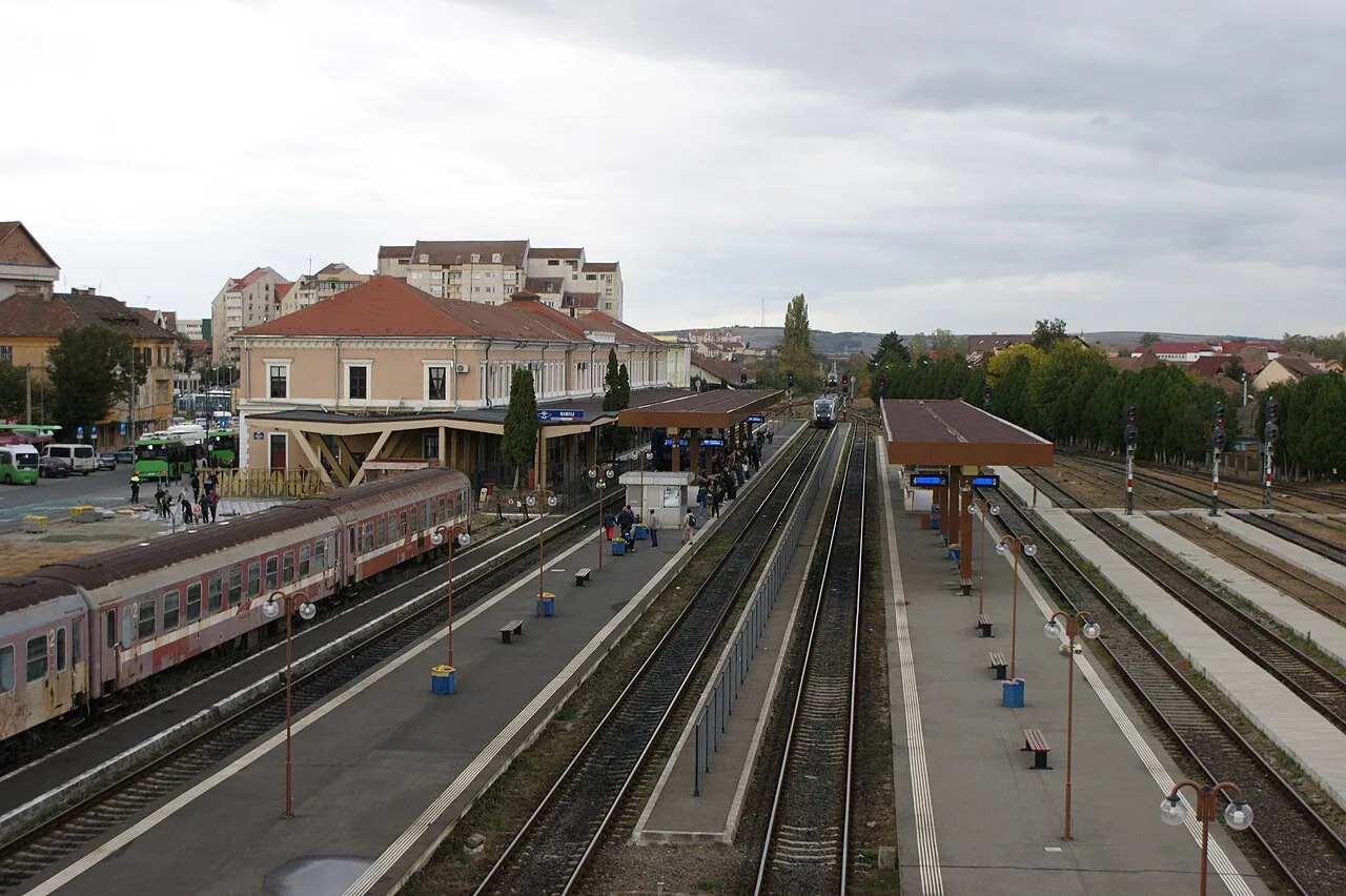 The elegant historic facade of Sibiu railway station with its arched windows and clock, where trains from Bucharest via Brasov arrive
