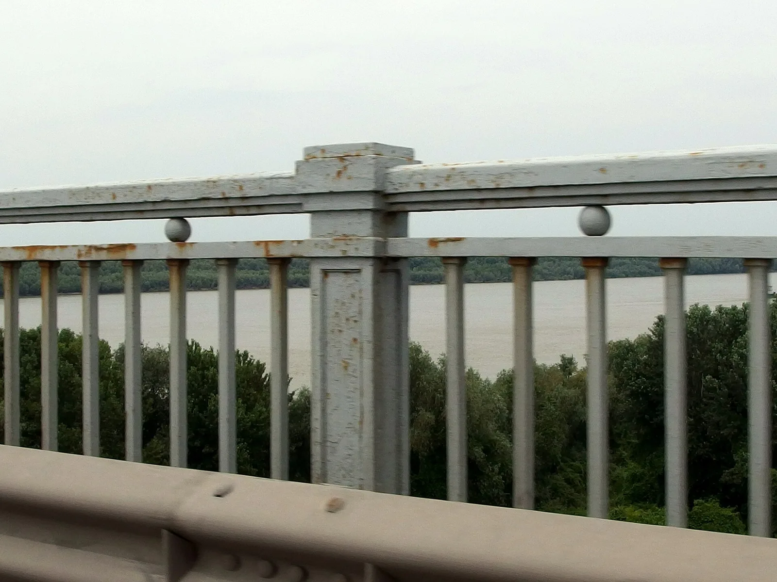 The rusty steel railings of the Danube Friendship Bridge seen from a vehicle crossing, the wide Danube and its wooded Bulgarian bank beyond