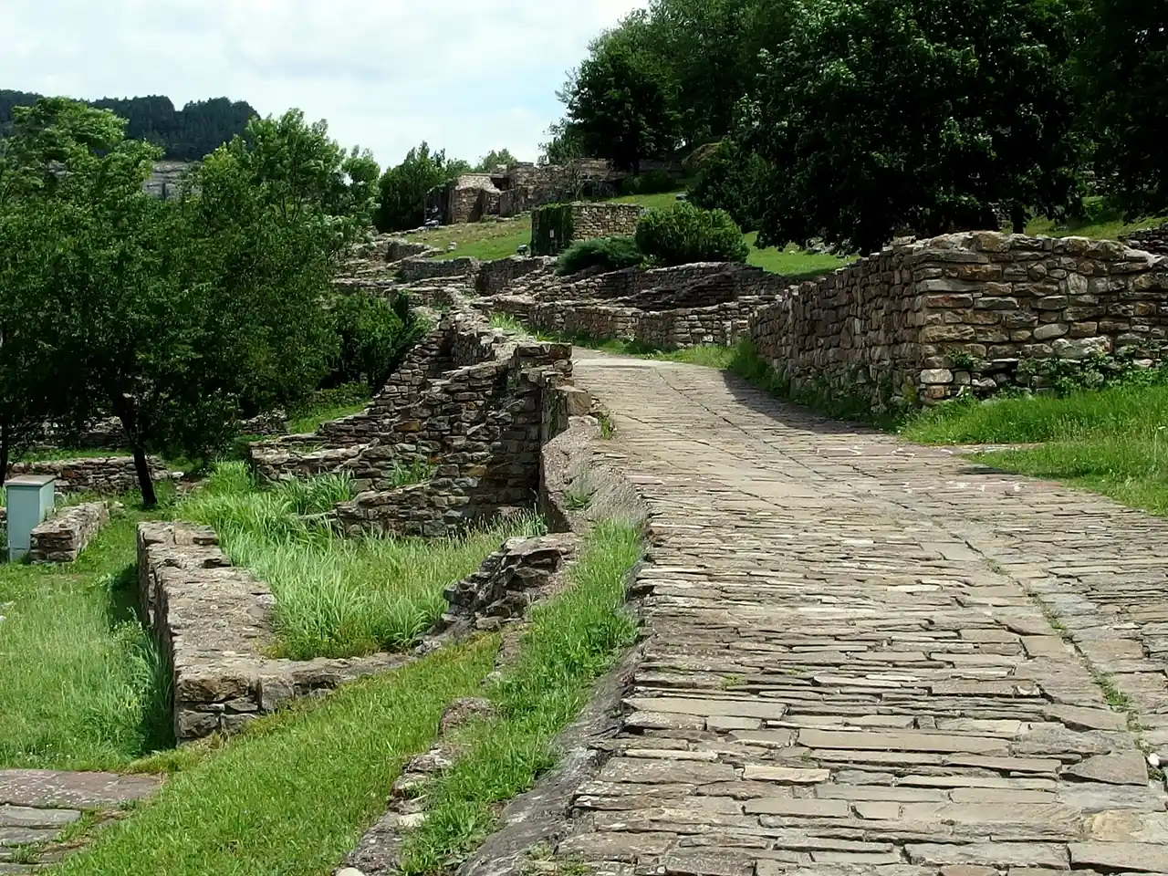 The stone ruins and paved path of Tsarevets fortress in Veliko Tarnovo, walls and green hillside under a bright sky