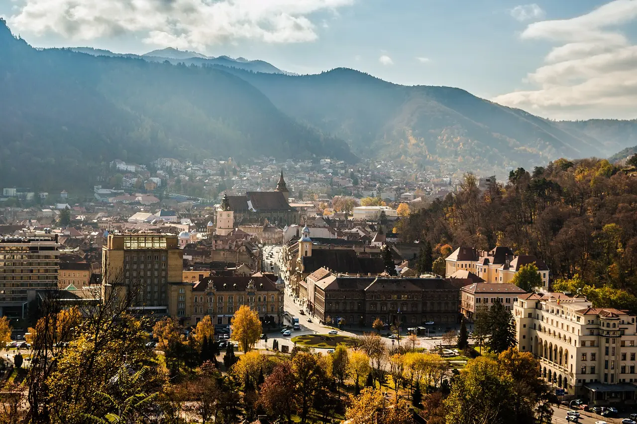 The red rooftops and Black Church of Brasov old town filling a valley bowl below the wooded Carpathian mountains in autumn