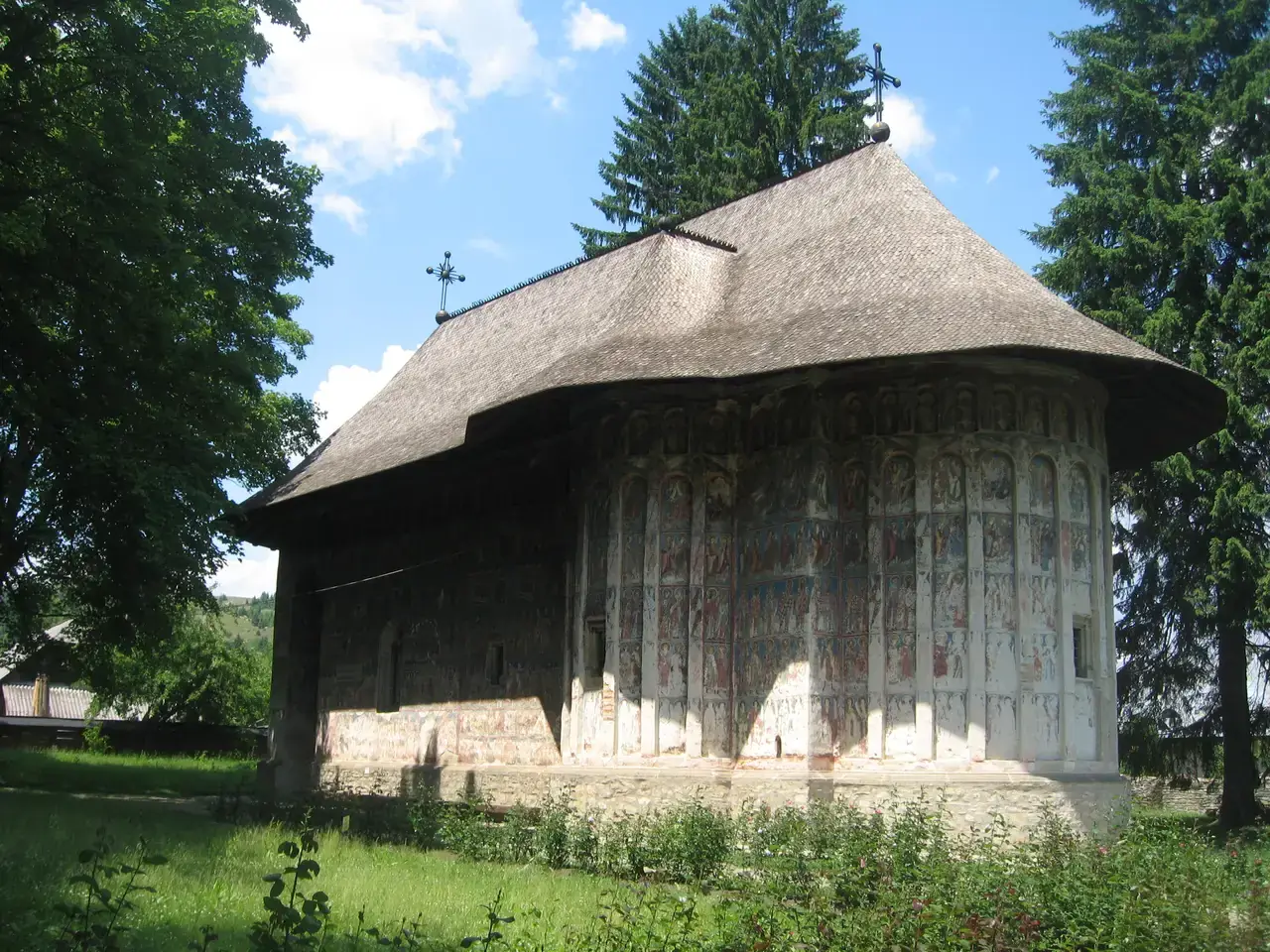 Humor Monastery church with faded exterior frescoes and a tall shingled roof among trees