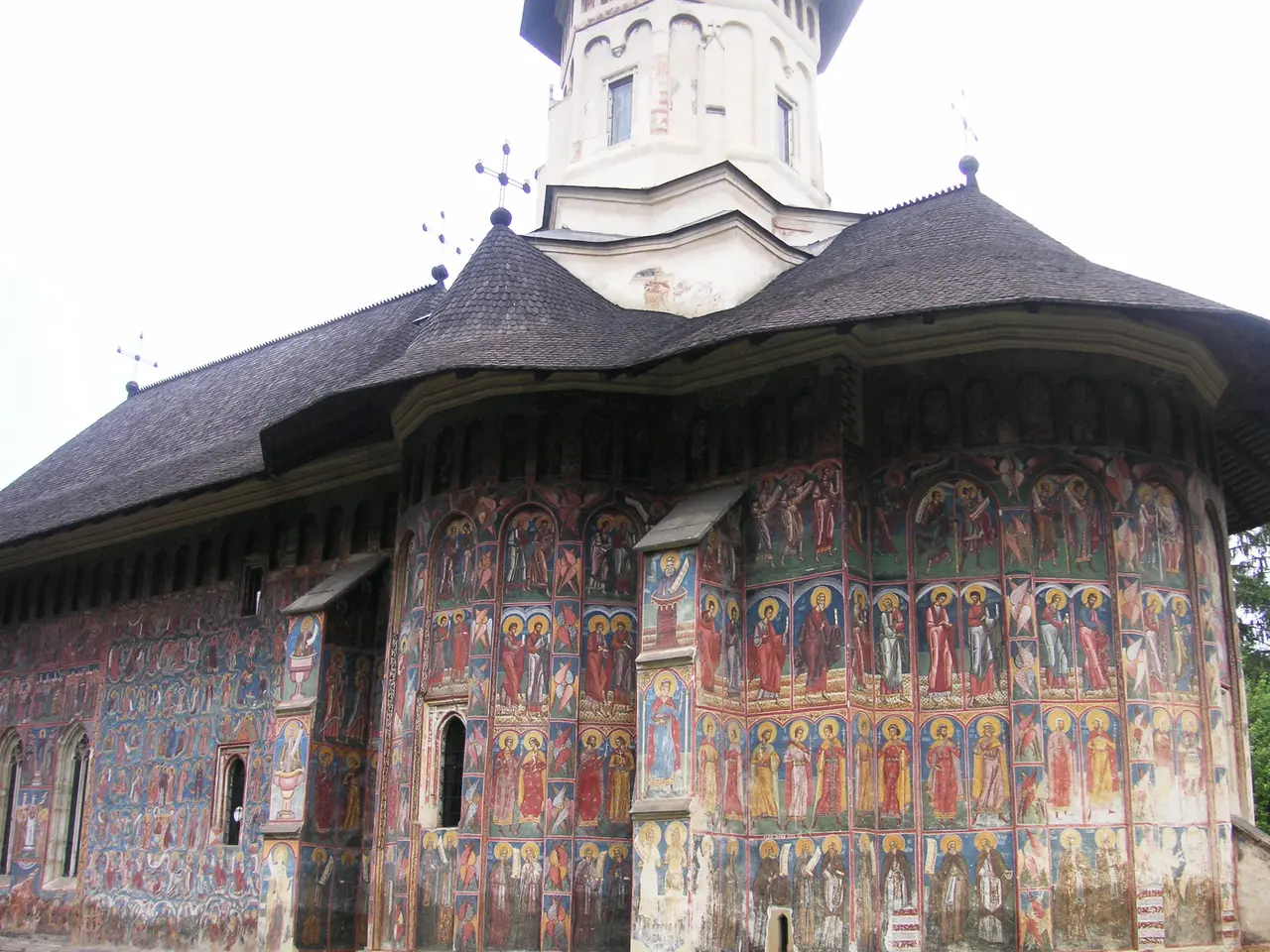 Moldovita Monastery church: exterior walls densely covered with colourful frescoes of saints under a broad shingled roof