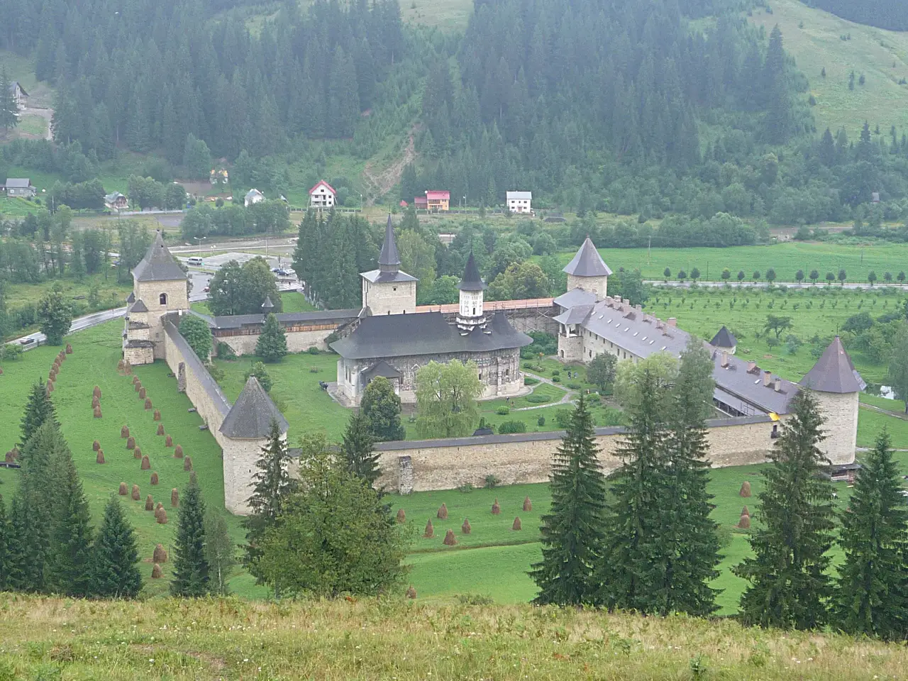 Aerial view of Sucevita Monastery: a fortified square of stone walls and corner towers around a painted church in a green valley