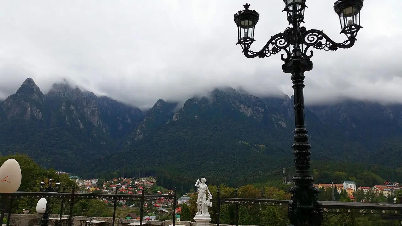 The view from the Cantacuzino terrace across a marble statue and an ornate lamppost to the cloud-wrapped peaks of the Bucegi mountains above Busteni