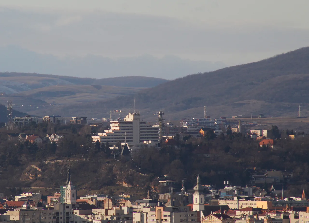 View over the rooftops of Cluj-Napoca toward the low wooded hills that ring the city