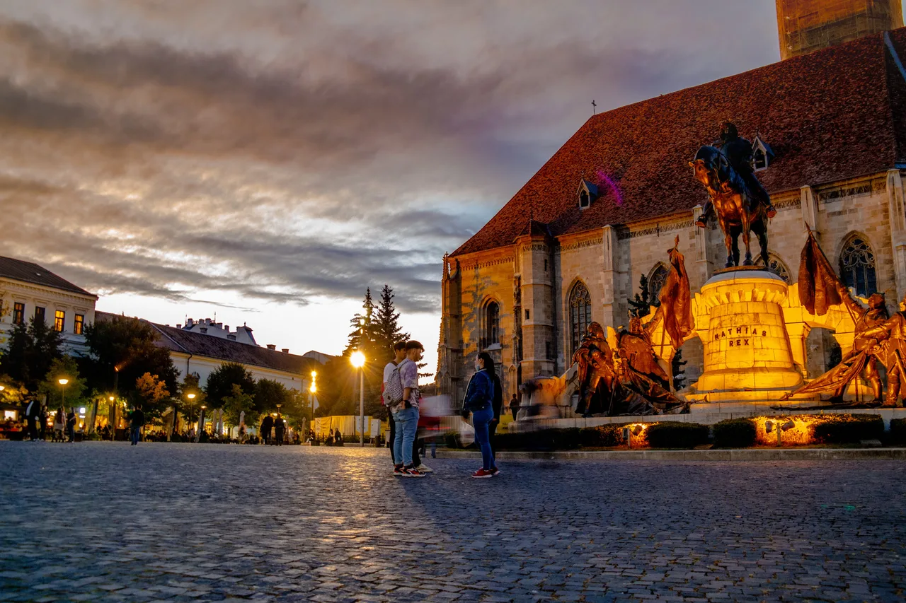 Union Square in Cluj-Napoca at dusk, St Michael's Church and the floodlit Matthias Corvinus statue glowing above the cobbles