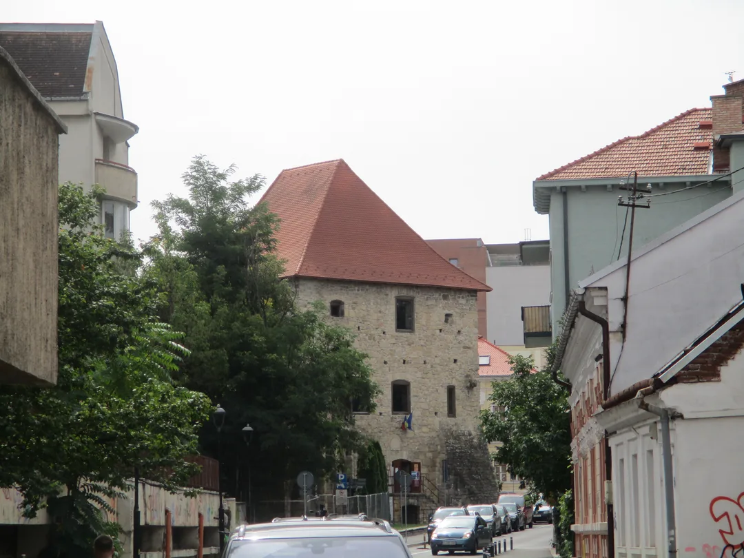 The Tailors' Bastion in Cluj-Napoca, a tall medieval stone tower with a steep red roof, seen from a street below