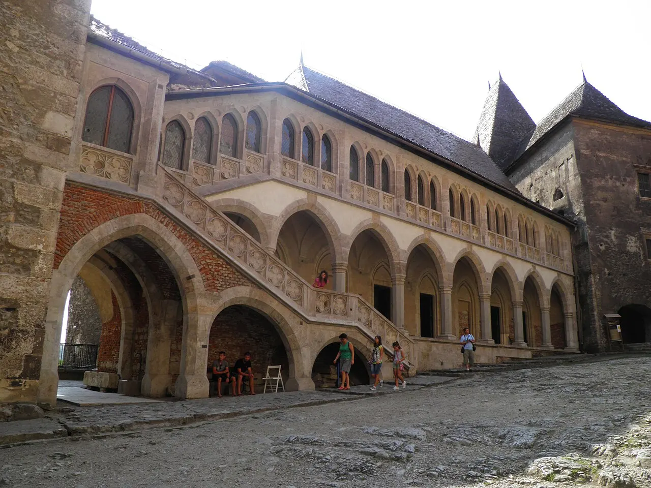 The inner courtyard of Corvin Castle showing a two-storey stone loggia with Gothic arches and an external staircase