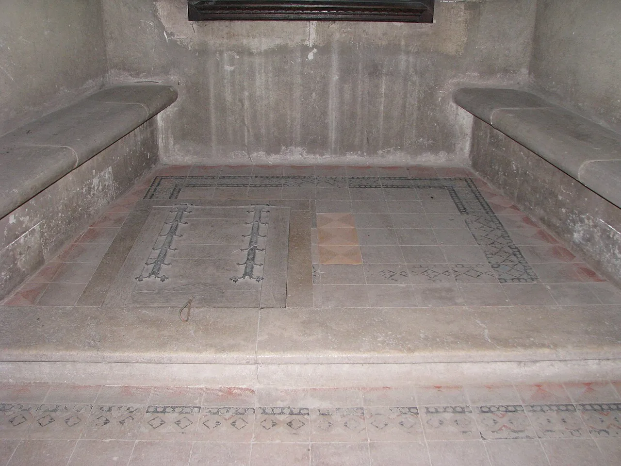 A stone window alcove with built-in benches and a patterned tiled floor inside Corvin Castle