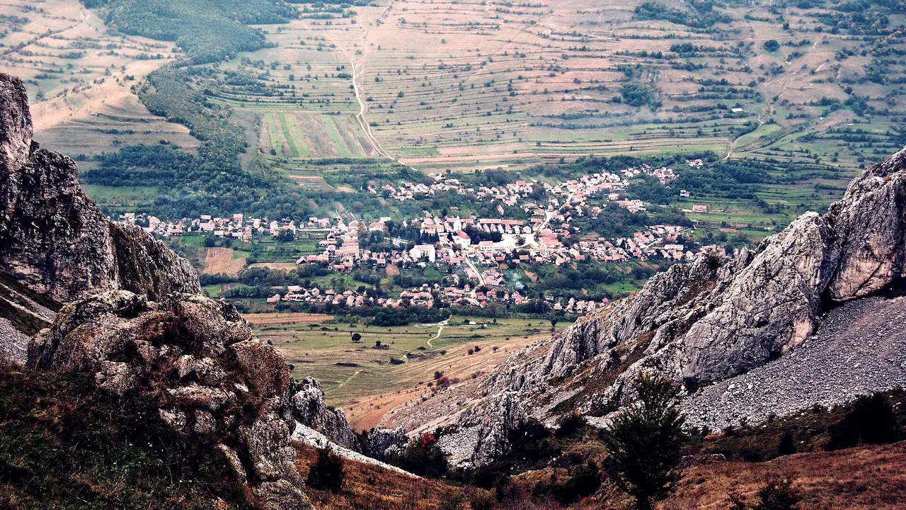 Rimetea village in a Transylvanian valley, red roofs clustered below limestone cliffs, seen from the hiking trail above