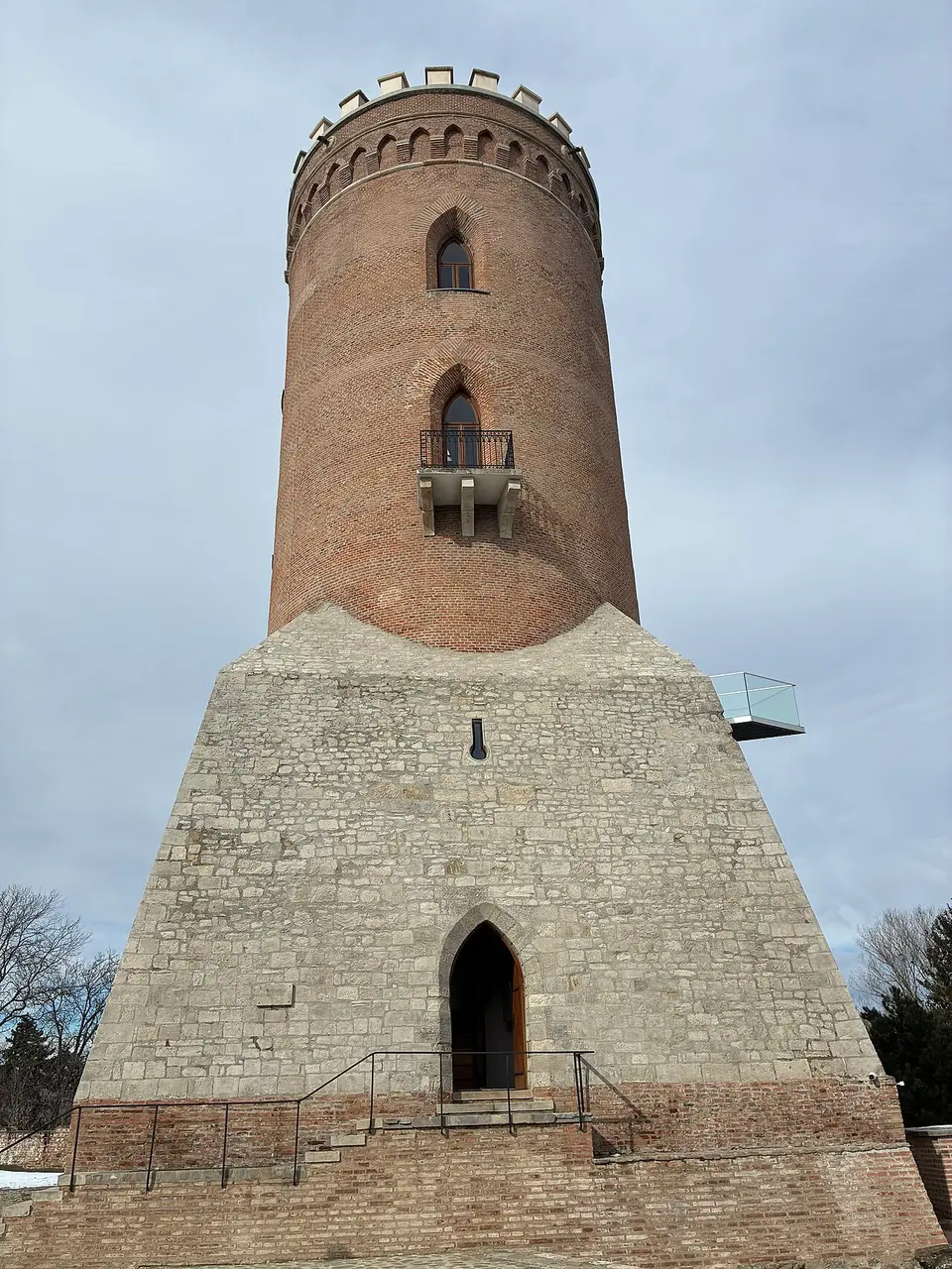 The brick Chindia Tower rising from its stone base at the Princely Court in Targoviste, with a Gothic arched doorway at ground level