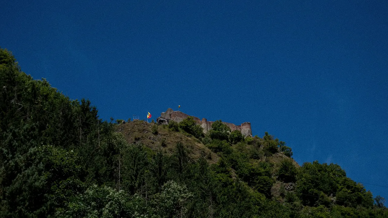 The ruined walls and tower of Poenari Castle on a wooded crag above the Arges valley, flying the Romanian flag, the fortress Vlad the Impaler actually held