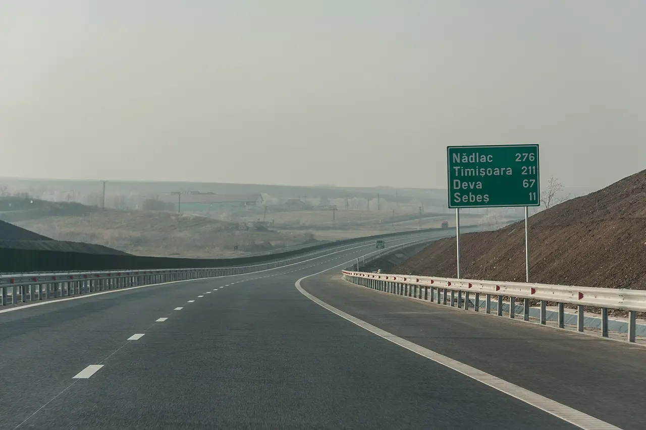 An empty stretch of the A1 motorway in Romania with a green distance sign reading Nadlac 276, Timisoara 211, Deva 67, Sebes 11