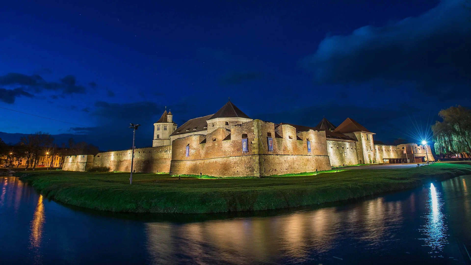 Fagaras citadel at dusk, its brick walls and red-tiled towers reflected in the still moat water