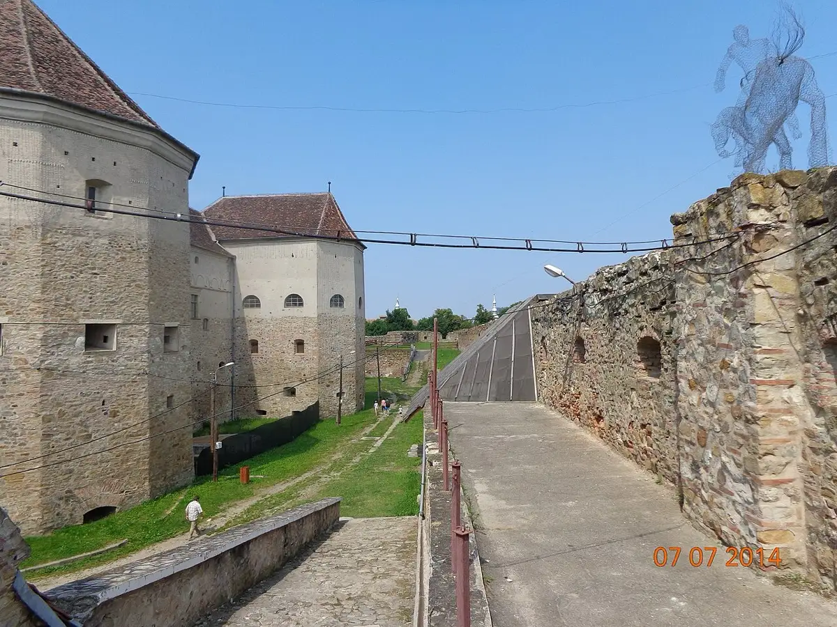 The grassy inner courtyard of Fagaras citadel, stone walls on all sides and a wooden reconstruction structure in the centre