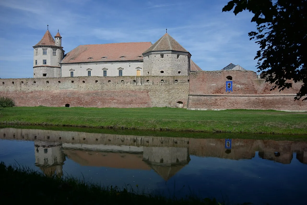 A long lateral view of Fagaras citadel showing the full length of its brick walls and moat from street level