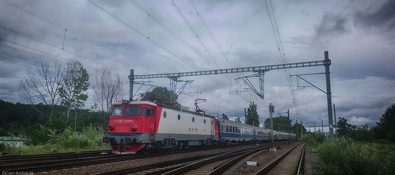 A CFR Calatori locomotive hauling passenger coaches on a Romanian main line, overhead electric wires above the track